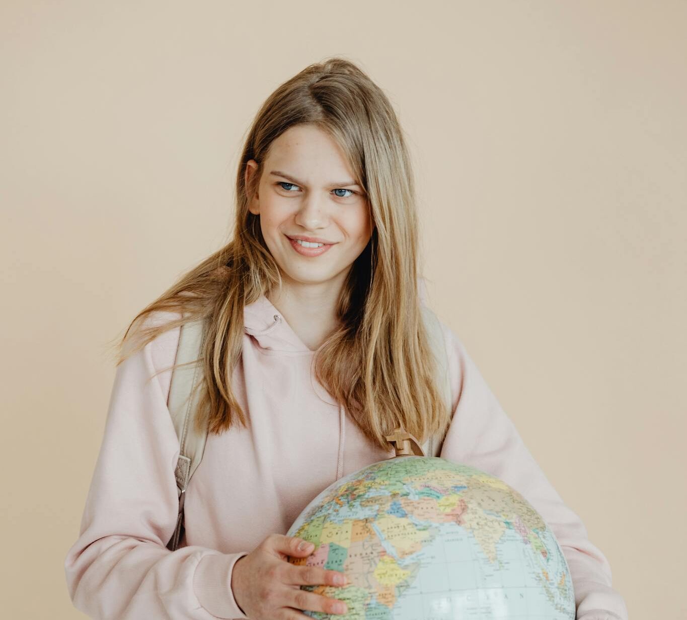 Teen girl in pink hoodie holding a globe, symbolizing education and geography.
